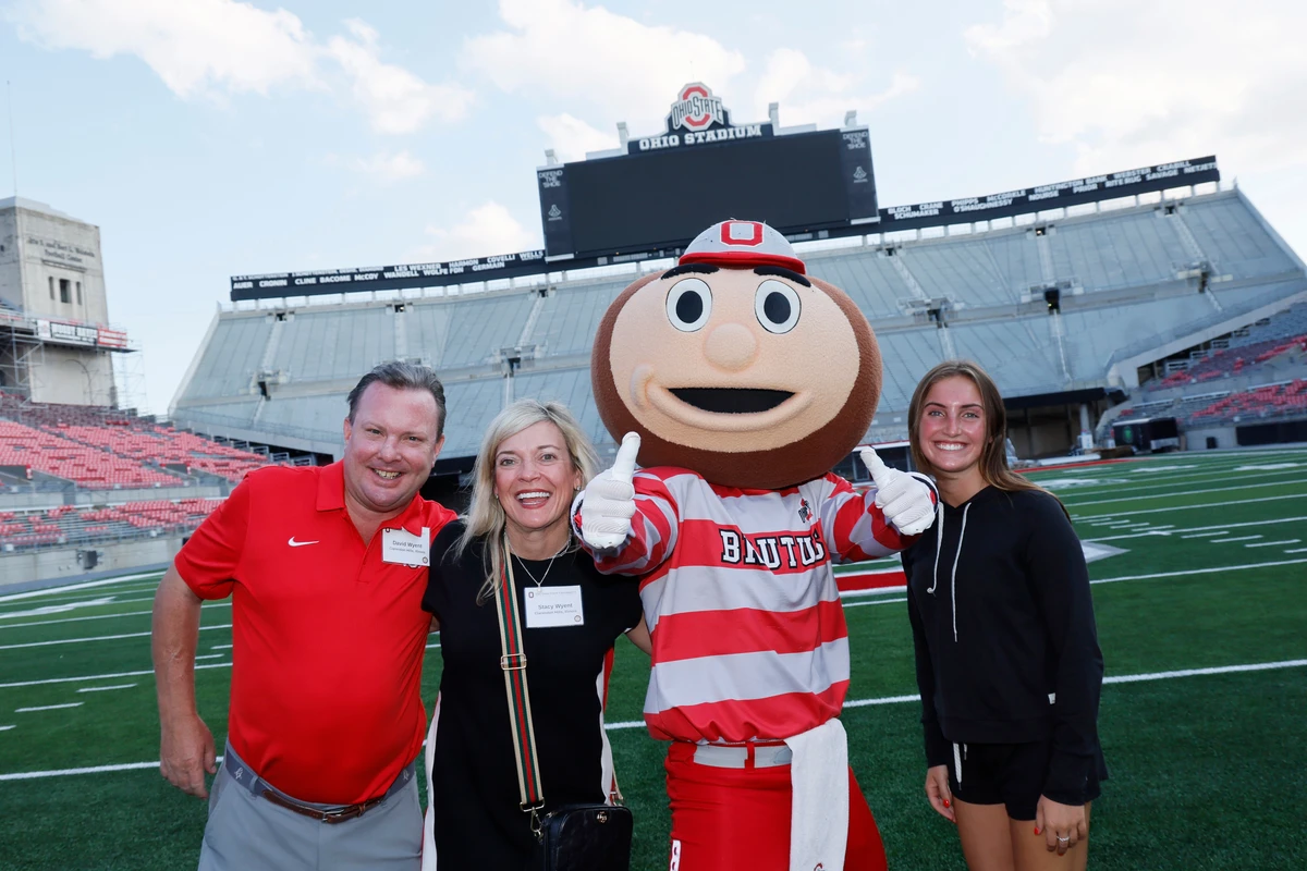 A group of people pose with a sports mascot on a football field.