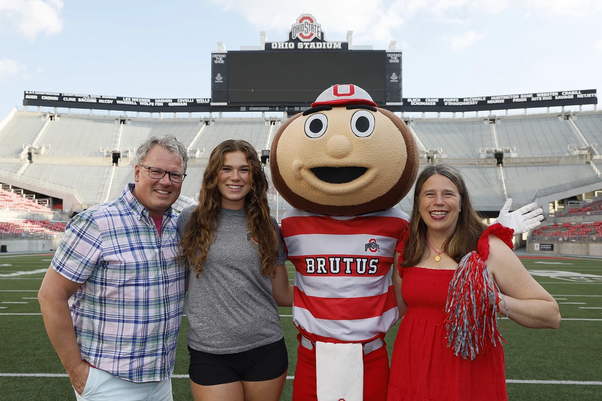 A group of people pose with a sports mascot on a football field.
